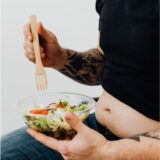 Man holding a bowl of salad with a wooden fork